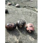 Trois pierres roulées rhodonite aux teintes rose et noir posées sur la roche en Bretagne, évoquant apaisement, ancrage et équilibre émotionnel.
