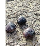 Trois pierres roulées de grenat almandin posées sur roche en Bretagne, pierres naturelles évoquant l’endurance, la stabilité émotionnelle et la puissance intérieure.