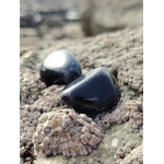 Pierre roulée d’obsidienne noire posée sur un rocher breton en lumière naturelle, pierre naturelle associée à la protection, à la stabilité intérieure et à la présence à soi.