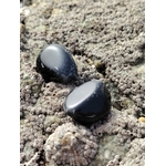 Pierre roulée d’obsidienne noire sur roche bretonne sous lumière naturelle, pierre naturelle évoquant la maîtrise de soi, la solidité émotionnelle et la protection subtile.