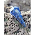 Pendule en lapis-lazuli bleu et doré posé sur un rocher marin couvert de coquillages en Bretagne, dans un décor naturel évoquant intuition, apaisement et clarté mentale.