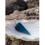 Pendule en apatite bleue posé sur un coquillage blanc, avec rocher texturé en arrière-plan, dans un décor naturel marin, évoquant intuition, apaisement émotionnel et clarté intérieure.