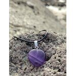 Pendentif cœur en améthyste sur cordon noir, posé sur la roche près de l’eau, dans une ambiance minérale apaisante évoquant sérénité, intuition et douceur intérieure.