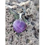 Pendentif cœur en améthyste sur cordon noir, posé sur la roche près de l’eau, dans une ambiance minérale apaisante évoquant sérénité, intuition et douceur intérieure.