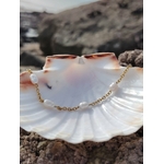 Bracelet eau douce en acier inoxydable et nacre posé sur un coquillage blanc en Bretagne, sur fond rocheux naturel, dans une lumière douce, évoquant sérénité et harmonie.