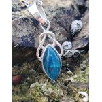 Pendentif elfique en apatite bleue et argent 925 photographié sur des rochers bretons au bord de l’eau, bijou en pierre naturelle évoquant la lucidité, l’expression sincère et l’apaisement.