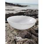 Bol en sélénite 15 cm photographié sur les rochers bretons au bord de l’eau, dans une ambiance douce et minérale, suggérant apaisement, purification et équilibre intérieur.