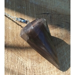 Pendule en pierre de lune noire posé sur une surface en bois clair, éclairé par une lumière chaude, avec chaîne argentée, dans une ambiance sobre et mystique évoquant intuition, ancrage et protection intérieure.