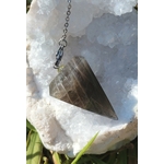 Pendule en pierre de lune noire sur un amas de quartz , baigné de lumière naturelle, dans une ambiance douce et épurée évoquant intuition, ancrage et protection intérieure.