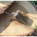 Pendule en pierre de lune noire posé sur une tranche de bois, éclairé par une lumière chaude, dans une ambiance naturelle et apaisante évoquant intuition, ancrage et protection intérieure.
