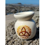 Brûleur en céramique blanc avec triquetra dorée, posé sur les rochers en Bretagne face à la mer, idéal pour fondants parfumés et bougie chauffe-plat, dans une ambiance d’harmonie et de douceur.