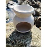 Vue arrière d’un brûleur en céramique blanc posé sur les rochers en Bretagne, avec ouverture pour bougie chauffe-plat et coupelle pour fondants, dans une ambiance douce et apaisante.