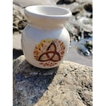 Brûleur en céramique blanc avec triquetra dorée, posé sur les rochers bretons près de l’eau, pour fondants parfumés et bougie chauffe-plat, dans une ambiance sereine et harmonieuse.