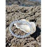 Bracelet Angel Aura 6 mm posé sur rochers en Bretagne avec coquillage blanc, perles irisées sur cristal de roche, douceur et apaisement