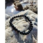 Bracelet tourmaline noire 6 mm posé sur galet brut gris, ambiance nature en Bretagne, calme du mental, enracinement et tenue émotionnelle