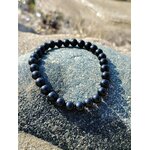 Bracelet tourmaline noire 6 mm posé en cercle sur galet gris brut, lumière naturelle, protection stable et solidité face aux tensions extérieures
