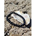 Bracelet tourmaline noire 6 mm autour d’un coquillage blanc sur écorce claire texturée, protection douce et maintien face aux ambiances lourdes