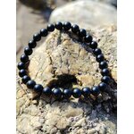 Bracelet tourmaline noire 6 mm en perles rondes sur pierre brute claire, ambiance minérale douce, courage calme et ancrage protecteur