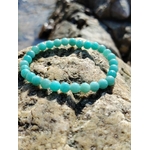 Bracelet amazonite 6 mm sur rocher brut dans un décor minéral, perles bleu lagon liées à la détente, à l’équilibre émotionnel et à la parole apaisée.