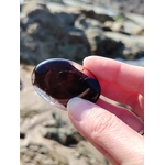 Main tenant un galet en quartz fumé devant les rochers bretons, pierre naturelle associée au discernement, à la stabilité émotionnelle et au retour au calme.
