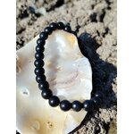 Bracelet shungite 6 mm posé sur coquillage clair avec roche texturée en fond, lucidité sobre, apaisement nerveux et protection rassurante