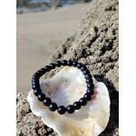 Bracelet shungite 6 mm sur coquillage blanc et bois flotté sculpté, lumière dorée en arrière-plan, relâchement profond et énergie plus posée