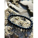 Bracelet shungite 6 mm noir intense en cercle sur roche claire et écorce sombre, présence ancrée, sobriété minérale et calme intérieur