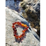 Bracelet en ambre pour bébé posé sur galet près de l’eau, fermoir de sécurité et nuances dorées, accessoire tendre au style naturel.