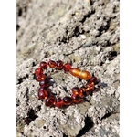 Bracelet bébé en ambre posé sur rochers bretons, bracelet enfant en ambre naturel aux tons chauds, photo nature au bord de mer
