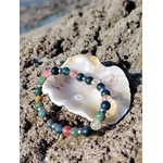 Bracelet chakra cœur en agate mousse et tourmaline melon d’eau présenté dans un coquillage sur rochers bretons, paix du cœur et relâchement émotionnel