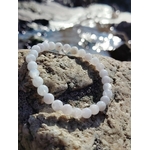 Bracelet en perles rondes bleu ciel marbré et blanches posé sur une écorce, avec coquillages flous en arrière-plan, photo Bretagne, évoquant la douceur, l’expression apaisée et l’harmonie intérieure