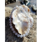Bracelet pierre de lune 6 mm blanc nacré irisé en perles rondes présenté sur un coquillage posé sur un rocher, dans une ambiance marine naturelle, évoquant l’intuition, la douceur