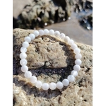 Bracelet en pierre de lune 6 mm posé sur les rochers en Bretagne près de l’eau, dans une ambiance douce et minérale évoquant intuition, sérénité