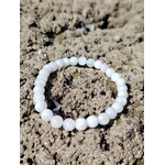 Bracelet pierre de lune 6 mm blanc nacré en perles rondes posé seul sur le sable, photo Bretagne, évoquant l’écoute intérieure, la sensibilité