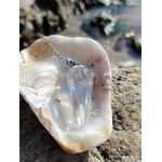 Pendule en cristal de roche présenté dans un coquillage sur la côte bretonne, entre roche et reflets marins, dans une atmosphère pure évoquant clarté, guidance et équilibre intérieur.