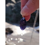 Main tenant un pendentif en iolite ou cordiérite au-dessus de l’eau en Bretagne, bijou en pierre naturelle associé à la fluidité intérieure, au recentrage et à la sérénité.