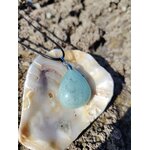 Pendentif en aigue-marine sur cordon noir, présenté dans un coquillage sur rochers en Bretagne, pierre naturelle associée à la sérénité, à la clarté émotionnelle et à la douceur océane.