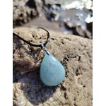 Pendentif en aigue-marine sur cordon noir, posé sur rochers en Bretagne au bord de l’eau, pierre naturelle associée au lâcher-prise, à la fraîcheur émotionnelle et à la lucidité.