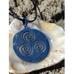 Pendentif Triskell bleu sur cordon noir présenté sur un coquillage parmi les rochers en Bretagne, bijou celtique au style minéral