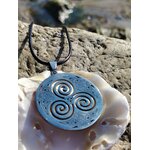 Pendentif Triskell bleu dans un coquillage sur rochers bretons, cordon noir et symbole celtique de vie en mouvement