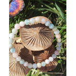 Bracelet Morganite 6 mm posé sur champignons en bois avec herbe verte, perles pastel rose, bleu et crème, bijou en pierre naturelle évoquant la douceur relationnelle, la délicatesse et la stabilité affective.