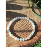 Bracelet Morganite 6 mm sur tranche de bois au soleil avec brins d’herbe, perles pastel aux nuances douces, bijou en pierre naturelle évoquant la tranquillité, l’amour de soi et l’apaisement émotionnel.