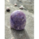 Lépidolite forme libre violette posée sur pierre humide près de l’eau, pierre naturelle évoquant l’apaisement, la souplesse émotionnelle et la sérénité.