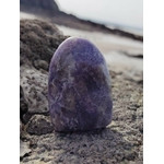 Lépidolite forme libre polie posée sur rocher en bord de plage, pierre naturelle reliée à la détente, au recentrage et à la douceur du cœur.