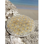 Plateau orgonite sélénite Fleur de Vie sur roche marine en Bretagne face à la plage, disque blanc lumineux au motif doré, clarté énergétique et apaisement intérieur.