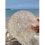 Plateau de rechargement orgonite sélénite photographié sur plage en Bretagne avec roche au premier plan, disque blanc lumineux et énergie apaisante, harmonie émotionnelle.