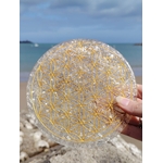 Plateau orgonite sélénite tenu en main face à la mer en Bretagne, disque blanc aux reflets nacrés et symbole Fleur de Vie, sérénité intérieure et équilibre vibratoire.