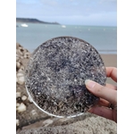 Plateau orgonite obsidienne noire tenu en main face à la mer en Bretagne, disque minéral gris noir poli, protection vibratoire et recentrage émotionnel.