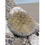 Plateau orgonite obsidienne noire avec Fleur de Vie dorée sur roche en bord de plage en Bretagne, disque de rechargement noir gris, apaisement émotionnel et ancrage profond.