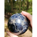 Sphère iolite ou cordiérite tenue en main en forêt en Bretagne, pierre bleu gris polie aux marbrures naturelles, recentrage et vision plus claire.